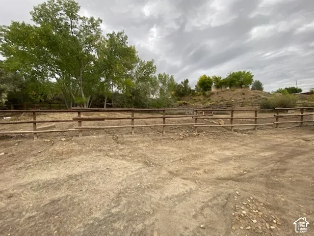 Fenced outdoor area with natural wood fencing, mature trees, and a dirt/gravel ground surface