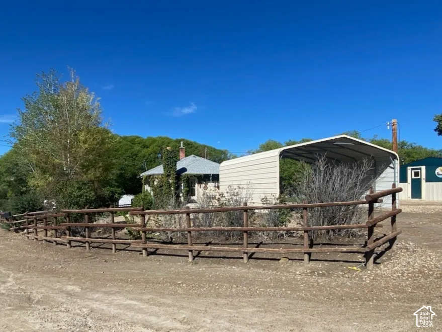 Wood fence defining a large gravel area, a detached carport, and a separate storage building.  Picture taken from gravel road.