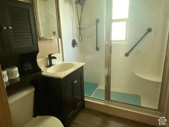 3/4 bathroom located by both bedrooms. Walk-in shower with sliding glass doors, built-in shower bench, dark wood-finish vanity with countertop sink, and wood-finish flooring