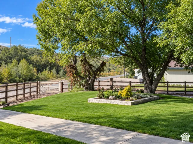 Manicured lawn with a stone-edged garden bed, mature shade trees, and a wood-post fence with wire mesh