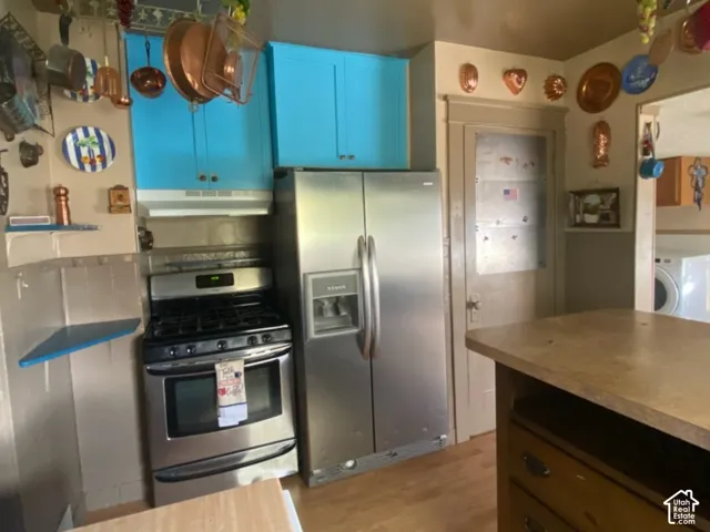 Stainless steel gas range and side-by-side refrigerator, bright blue upper cabinetry, and wood-finish flooring