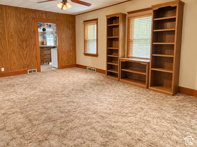 Built-in shelving and cabinetry, wood-paneled wall, ceiling fan with integrated lighting, and carpeted flooring