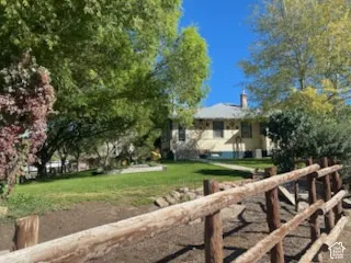 Expansive lawn with mature trees, a rustic wood fence, and a distant residence with a chimney
