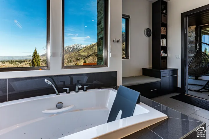 Built-in soaking tub with deck-mounted fixtures, large windows showcasing a mountain backdrop, and built-in cabinetry with open shelving