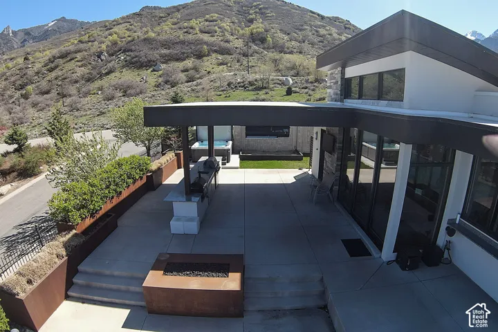 Expansive concrete patio featuring a built-in grill station, recessed hot tub, and a modern fire pit