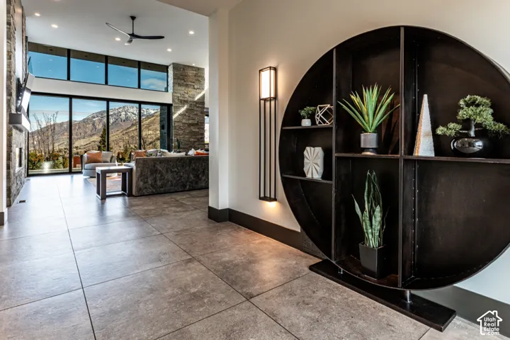 Large format tile flooring, stone accent wall, floor-to-ceiling windows, built-in circular shelving, and a modern ceiling fan
