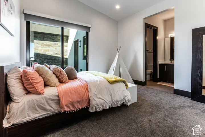 Floor-to-ceiling sliding glass doors, dark wood-finish bed frame, dark gray carpet, recessed lighting, and an adjacent bathroom with a dark vanity