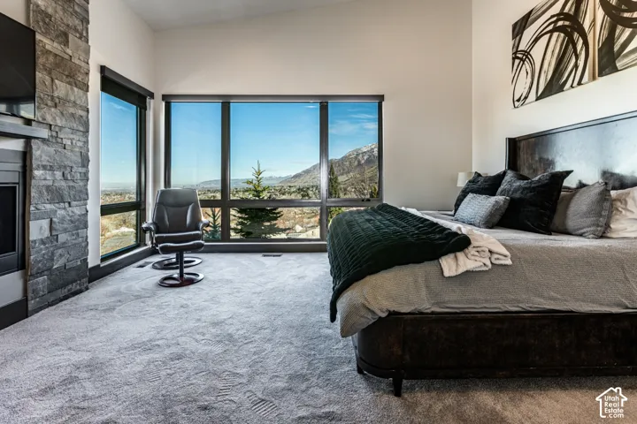 Floor-to-ceiling windows, stacked stone fireplace, vaulted ceilings, and light-toned carpeting