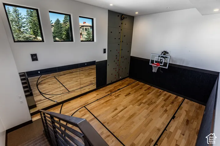 Dedicated recreation room featuring wood-finish flooring, black wainscoting, three large windows with natural light, a climbing wall, and a basketball hoop