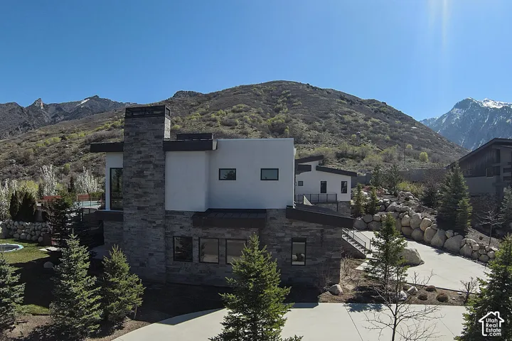 Contemporary architecture with stone and stucco exterior, prominent chimney structure, multiple window placements, and a paved driveway