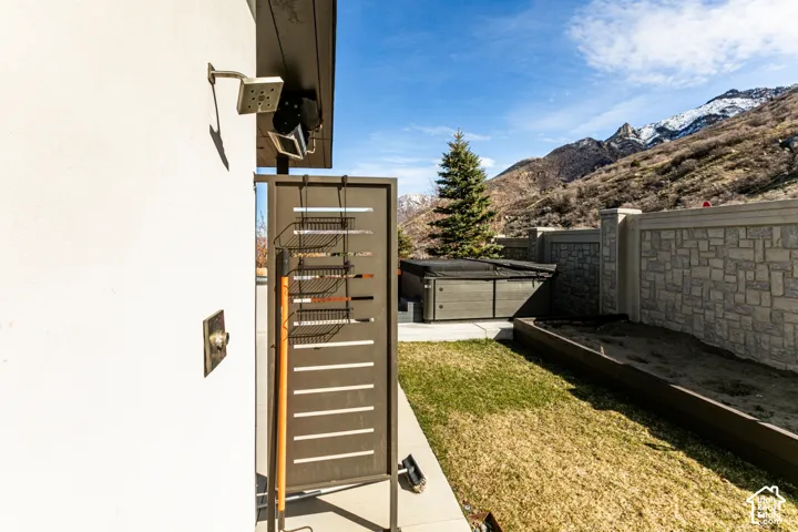 Modern side courtyard featuring a manicured lawn, horizontal wood-slat gate with stainless steel hardware, concrete block perimeter walls, and mountain backdrop with mature evergreen landscaping