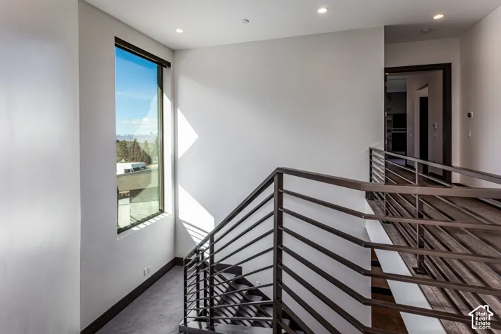 Modern staircase with metal railings, full-height window, recessed lighting, and wood-finish flooring