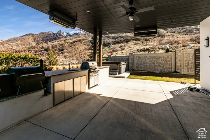 Expansive covered patio featuring an outdoor kitchen with built-in appliances, a ceiling fan, and a hot tub