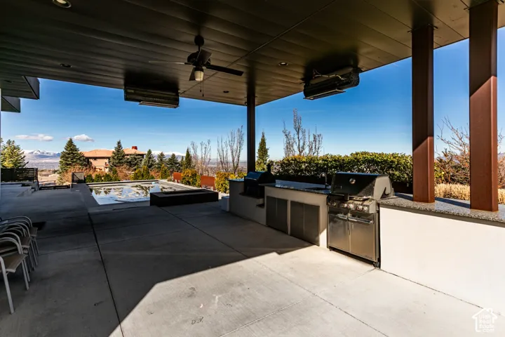 Expansive outdoor patio with concrete flooring, covered ceiling, built-in outdoor kitchen with stainless steel grill, and an integrated water feature