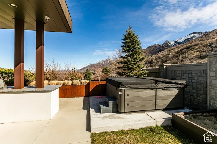 Outdoor patio with an integrated spa, concrete hardscaping, and a stone-clad retaining wall