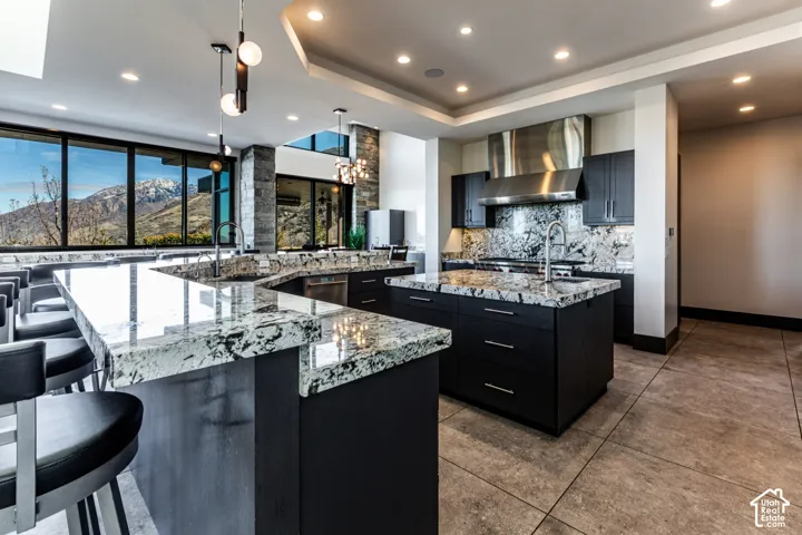 Expansive kitchen featuring a large island, premium stone countertops, stainless steel hood, recessed lighting, and large windows