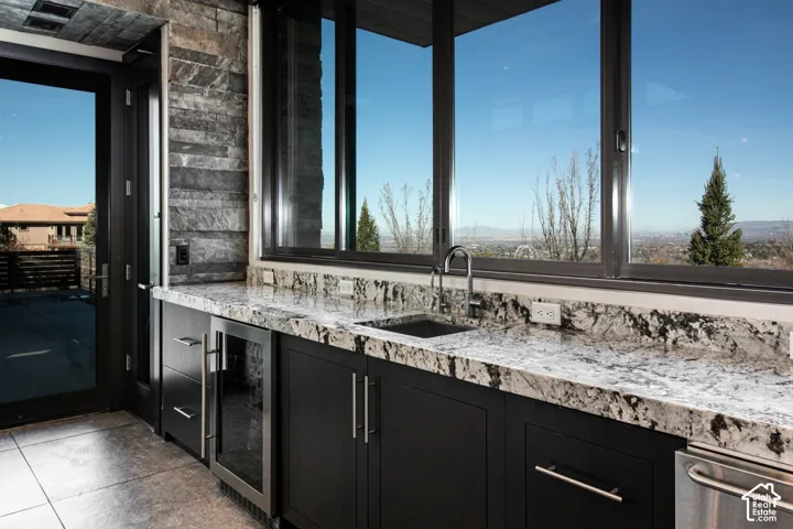 Integrated wet bar with a stainless steel sink, sleek dark cabinetry, premium stone countertops, and an under-counter beverage cooler