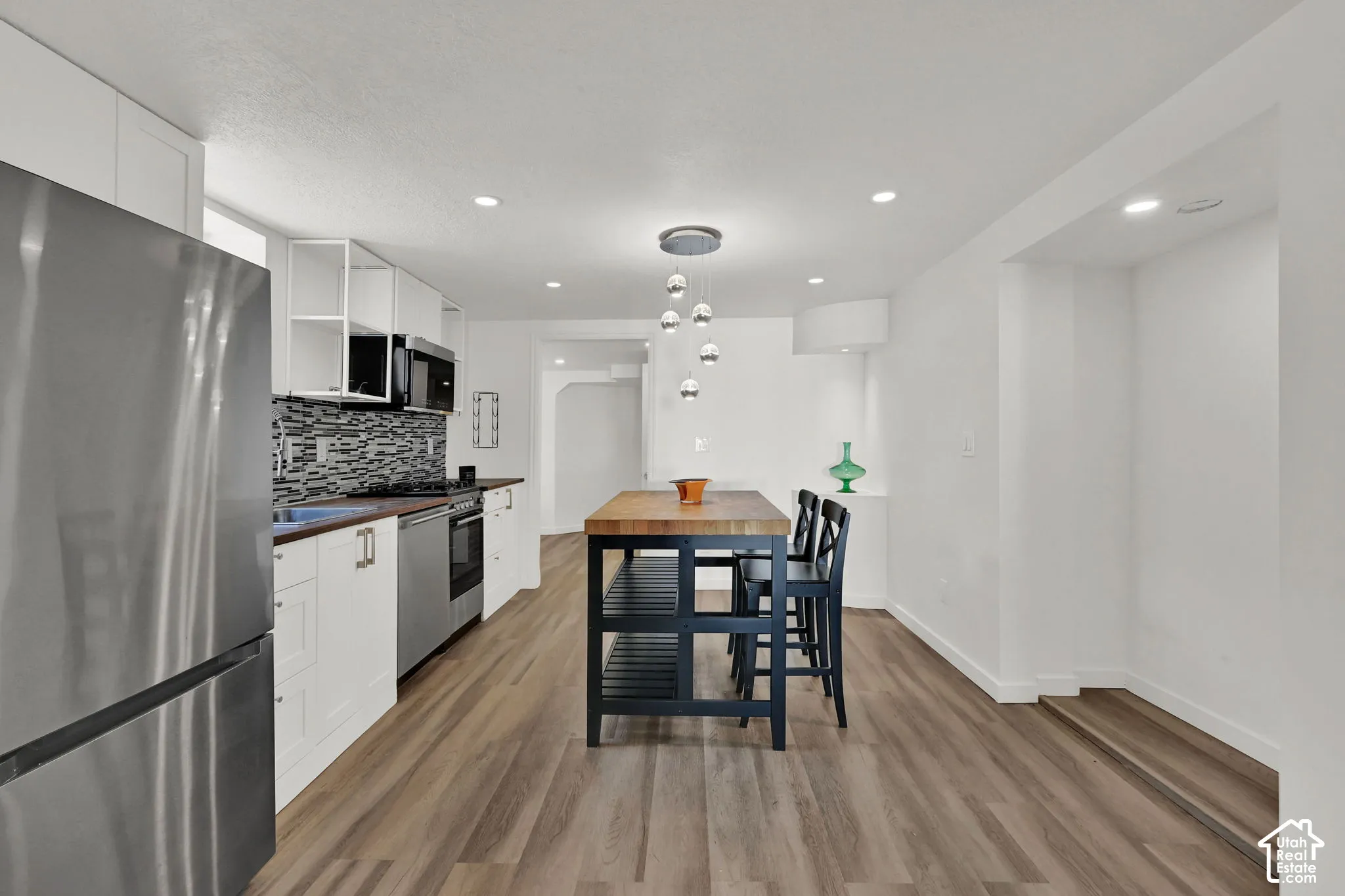 Modern kitchen with wood-finish flooring, white cabinetry, stainless steel appliances, and a mosaic tile backsplash