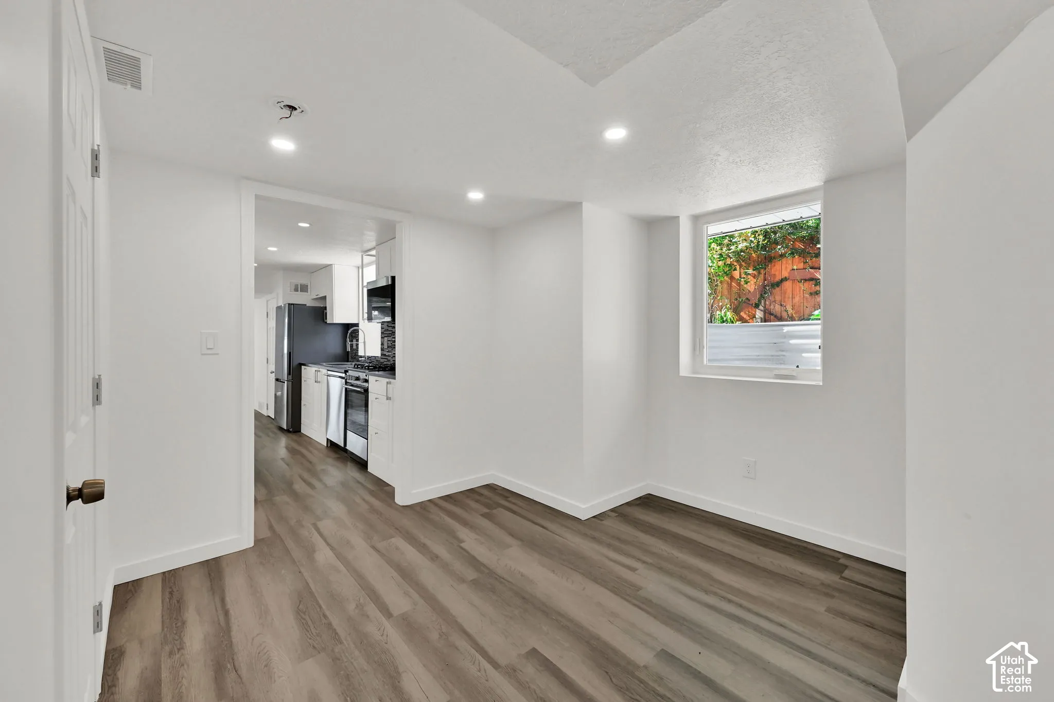 Recessed lighting, wood-finish flooring, white walls, and a visible window