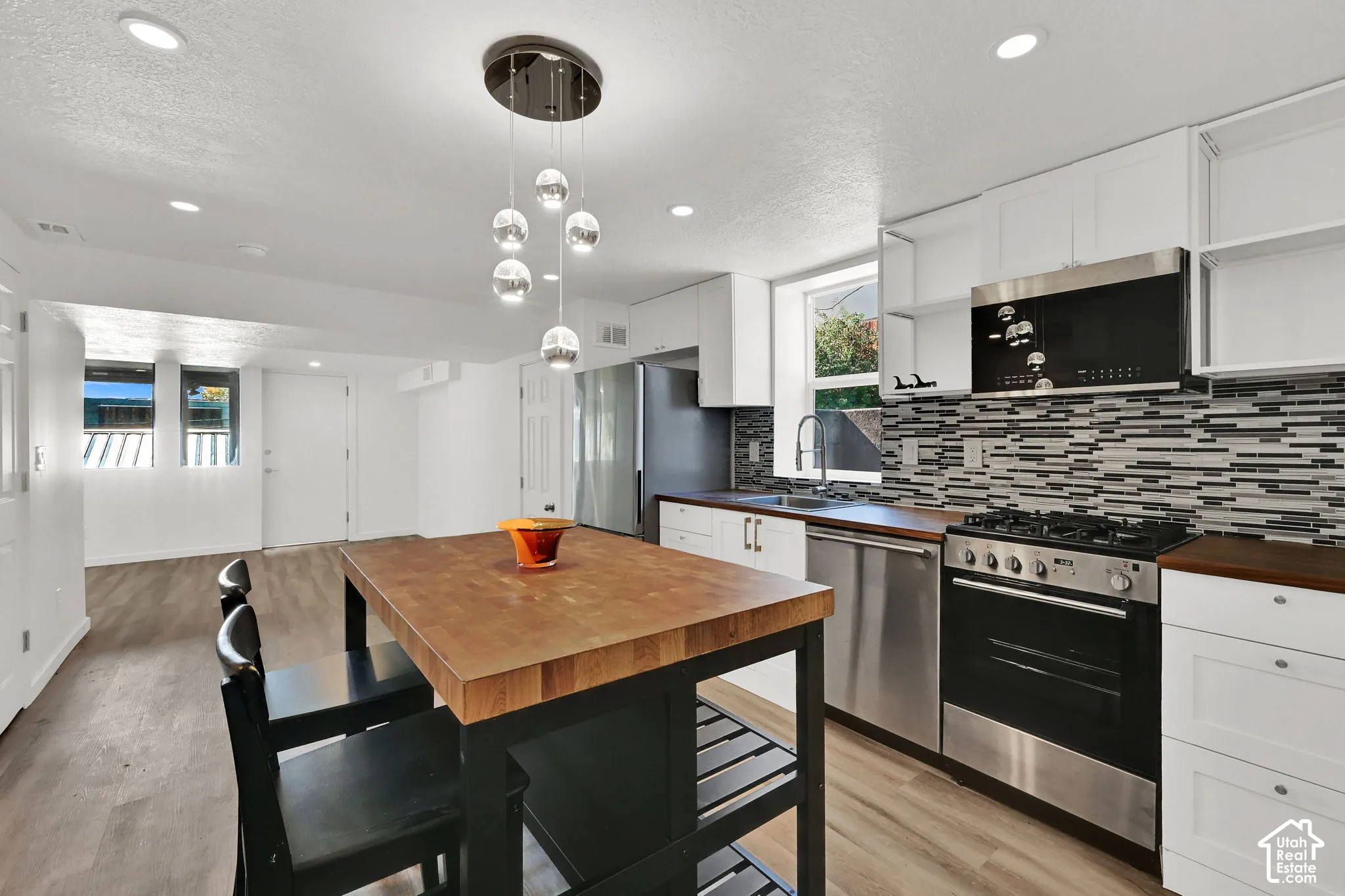 Kitchen featuring stainless steel appliances, mosaic tile backsplash, solid wood countertops, white cabinetry, and wood-finish flooring