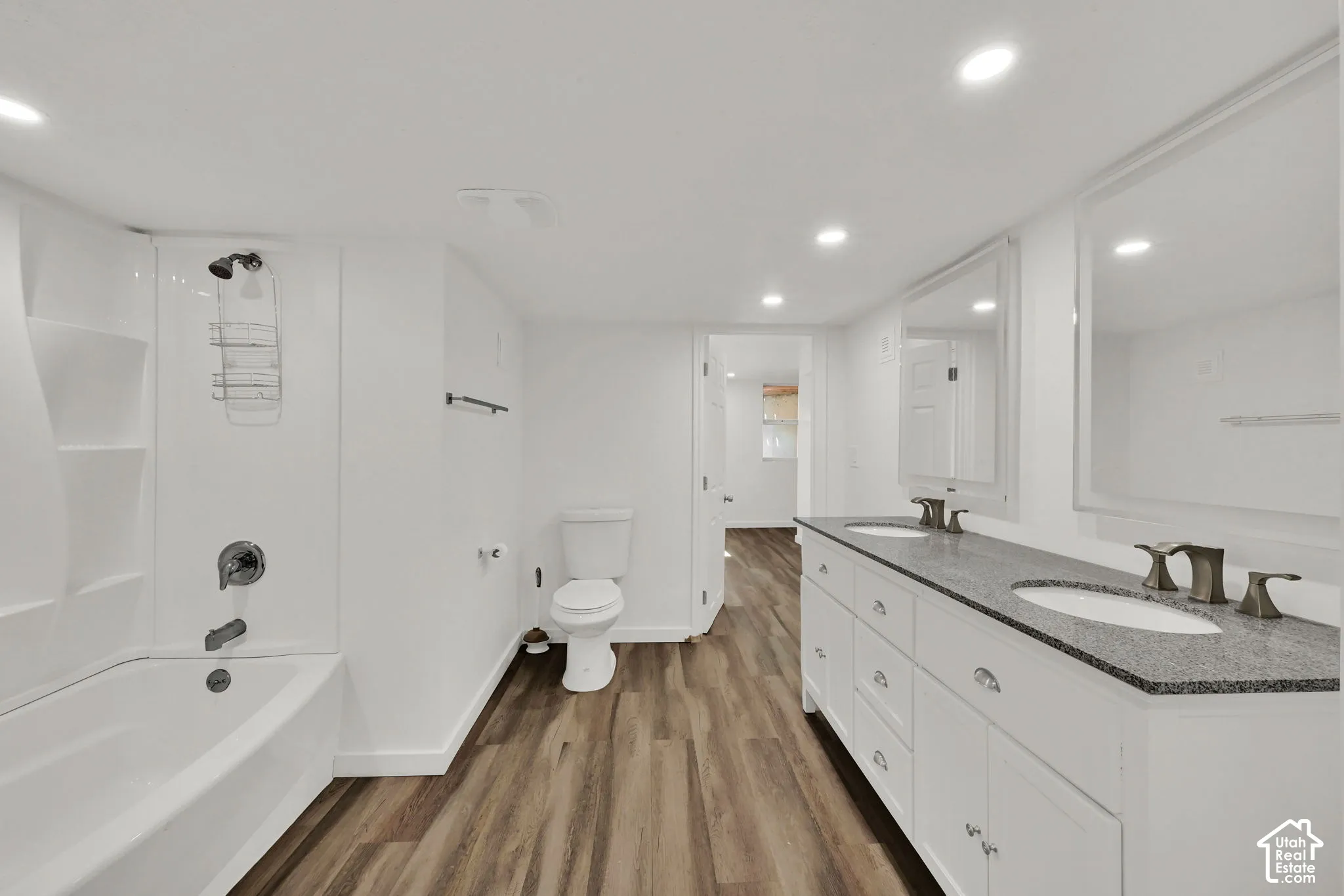 Double vanity with stone countertop, white shaker cabinetry, wood-finish flooring, recessed lighting, and a white tub/shower combination