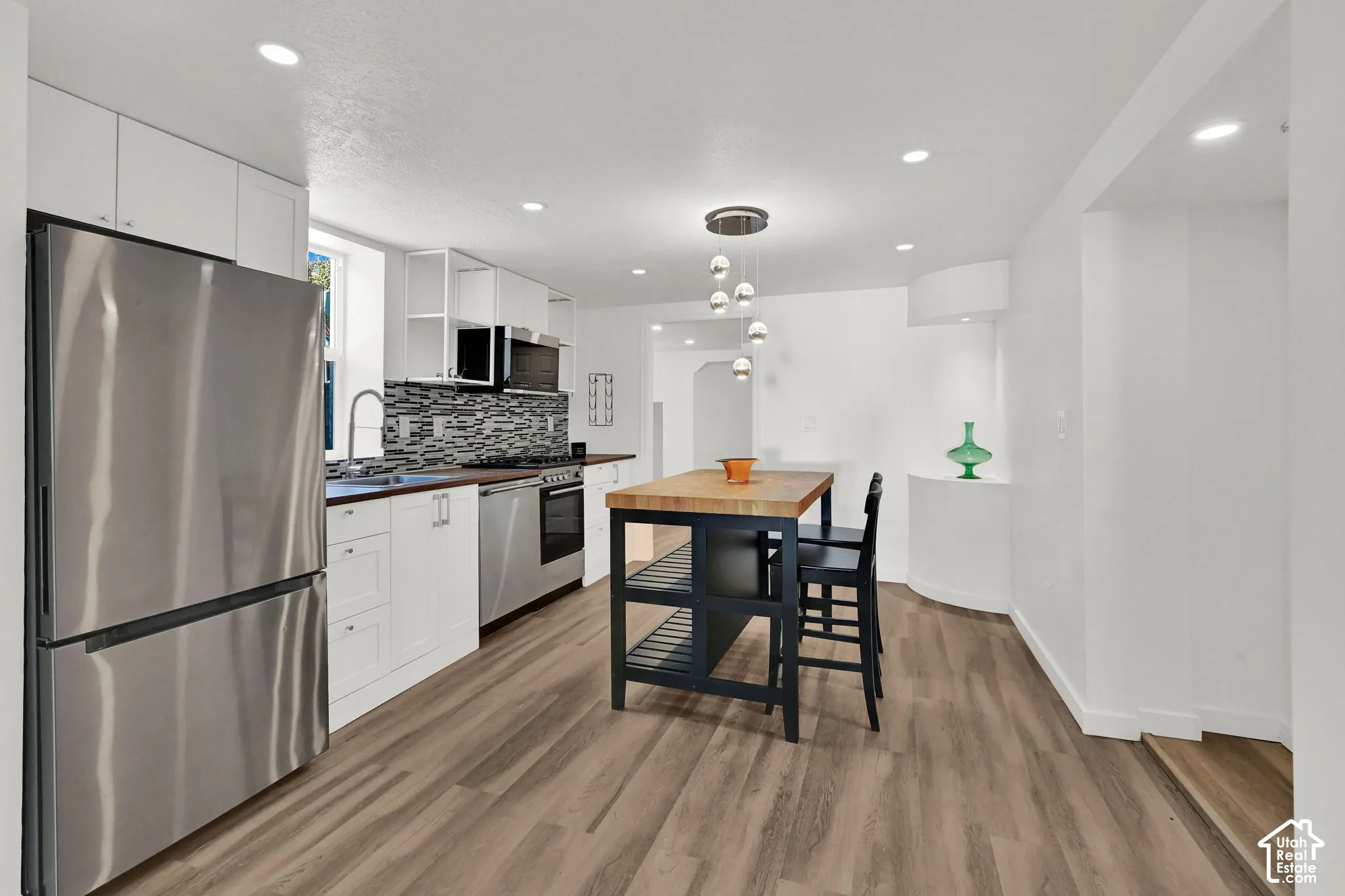 White cabinetry, stainless steel appliances, wood-finish flooring, a butcher block island with integrated shelving, and recessed lighting