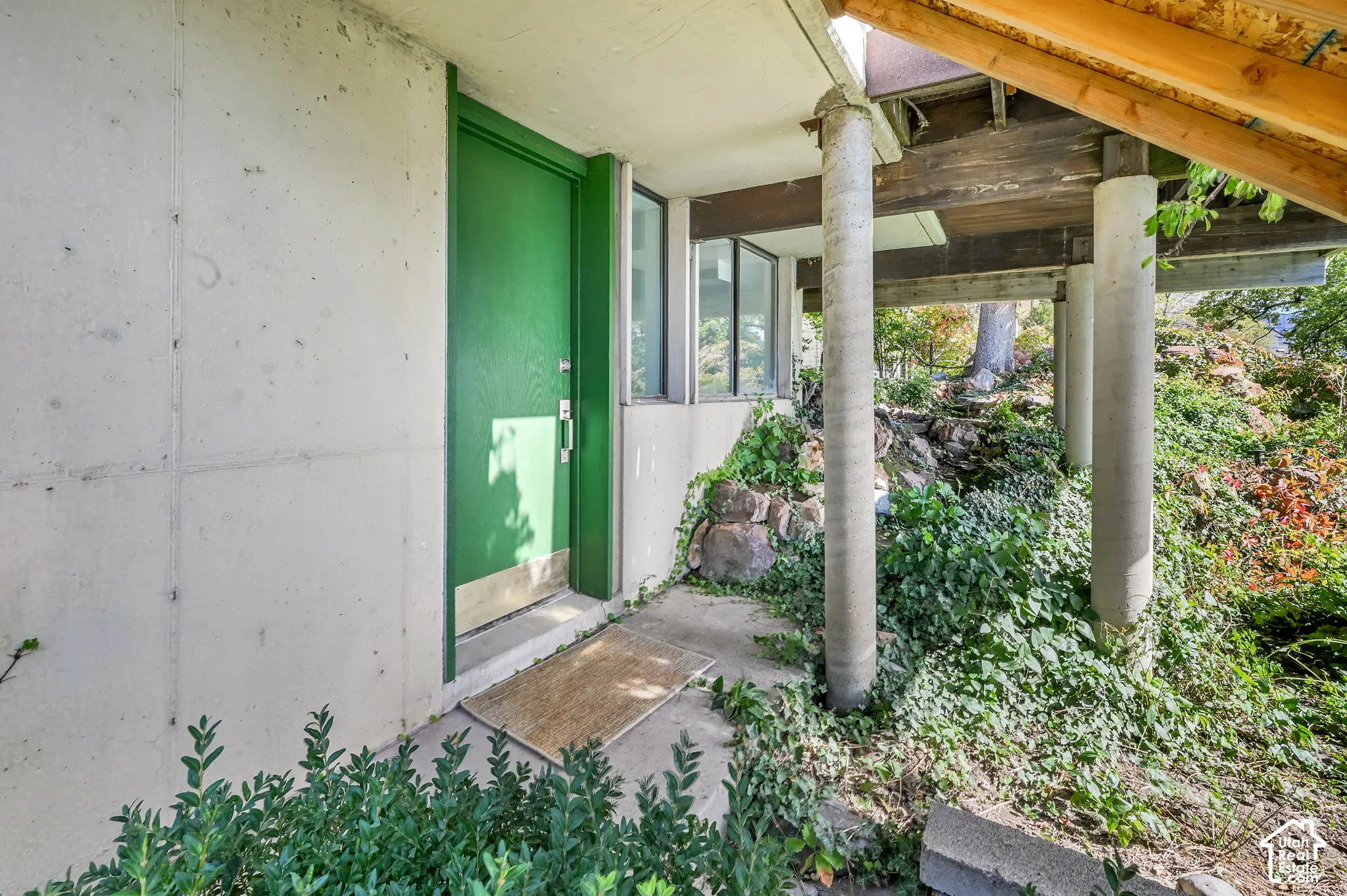 Concrete exterior with a vibrant green entry door, concrete columns, wood beams, and established landscaping
