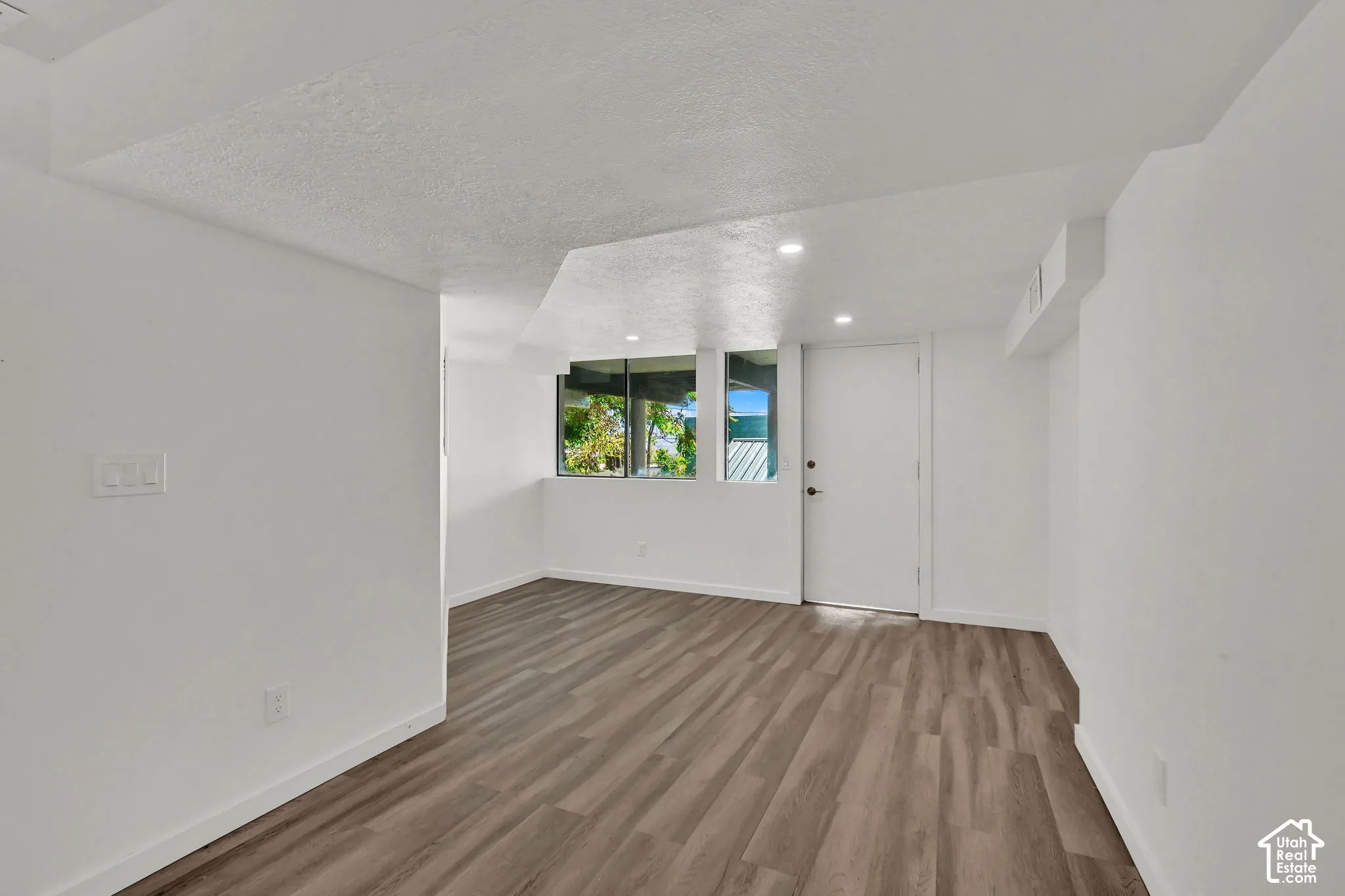 Recessed lighting, wood-finish flooring, multiple windows, and a white door with black hardware