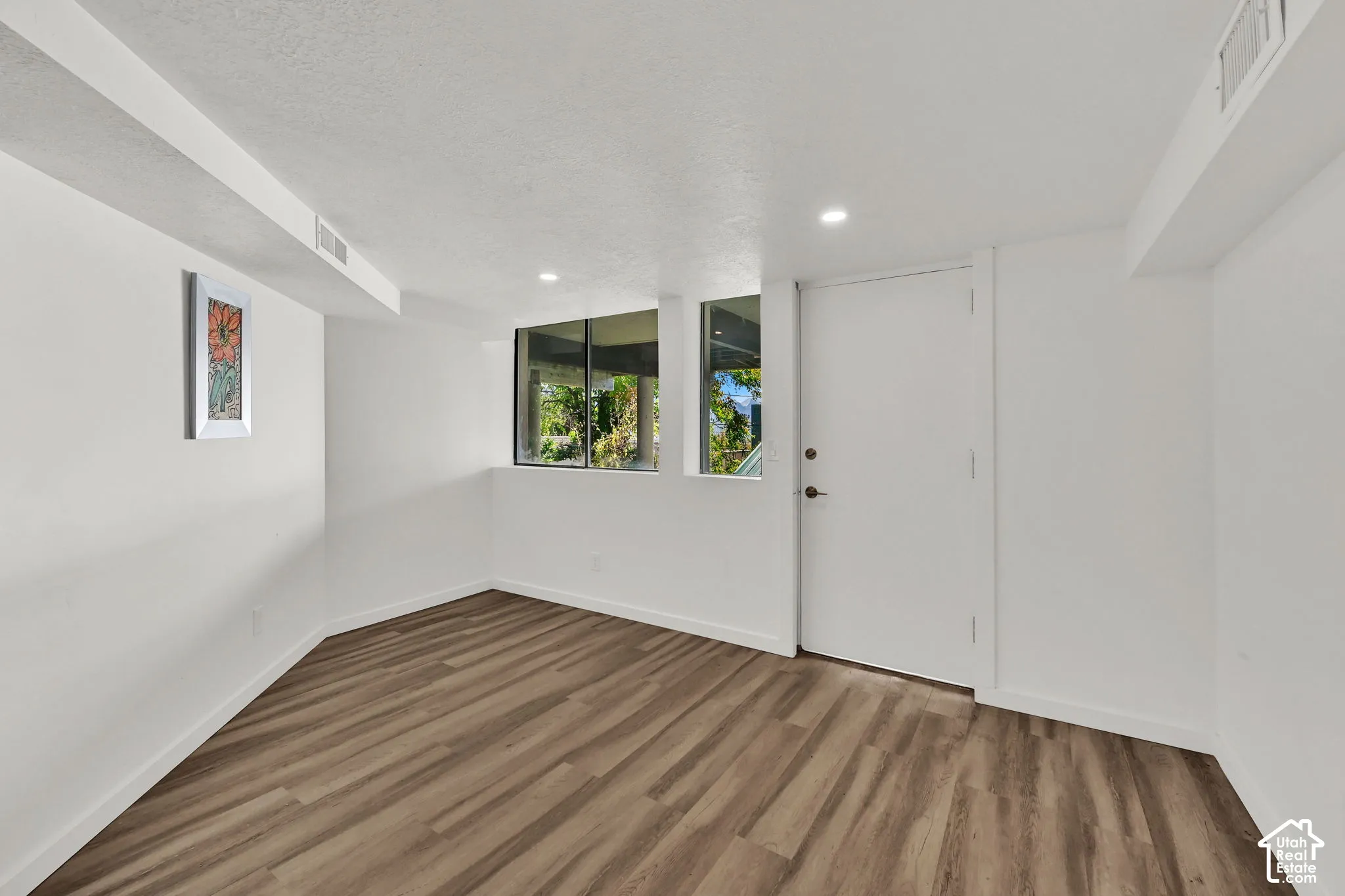 Wood-finish flooring with white walls, recessed lighting, and large windows