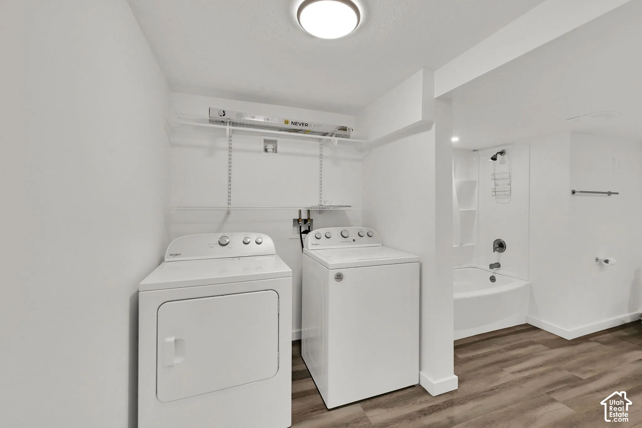 Laundry area with wire shelving, washer and dryer, wood-finish flooring, and a built-in tub with a shower fixture