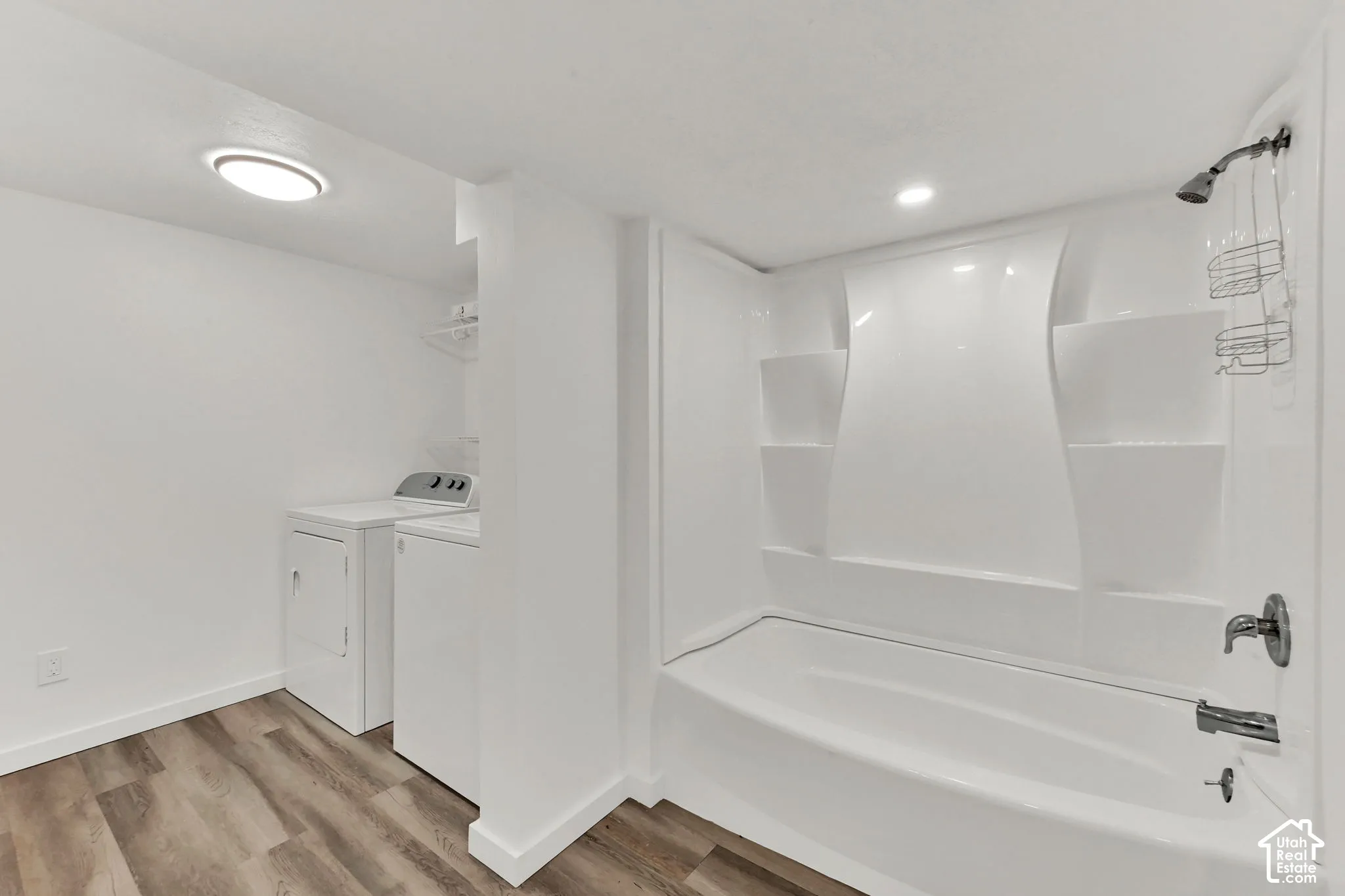 White fiberglass tub with integrated shelving, chrome shower fixtures, and wood-finish flooring