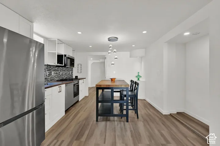 Modern kitchen with wood-finish flooring, white cabinetry, stainless steel appliances, and a mosaic tile backsplash