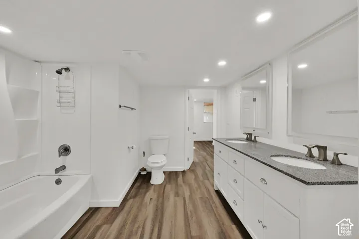 Double vanity with stone countertop, white shaker cabinetry, wood-finish flooring, recessed lighting, and a white tub/shower combination