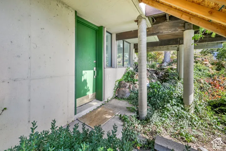 Concrete exterior with a vibrant green entry door, concrete columns, wood beams, and established landscaping
