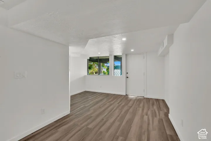 Recessed lighting, wood-finish flooring, multiple windows, and a white door with black hardware