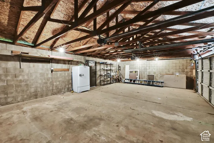 Exposed rafter ceiling, concrete block walls, concrete flooring, overhead lighting, and an automated garage door