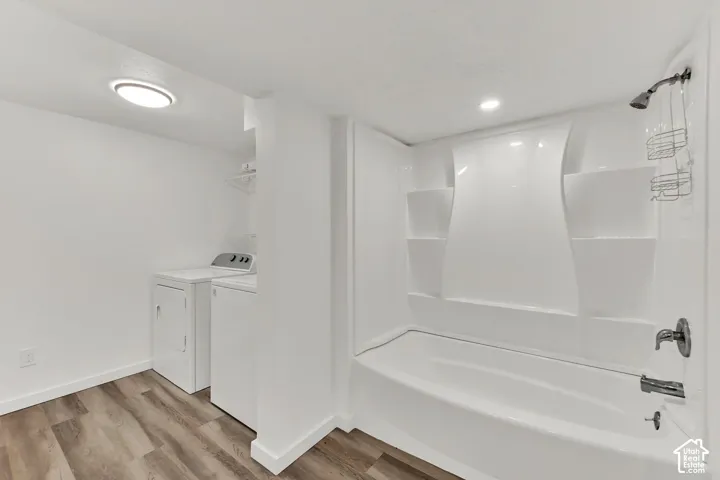 White fiberglass tub with integrated shelving, chrome shower fixtures, and wood-finish flooring