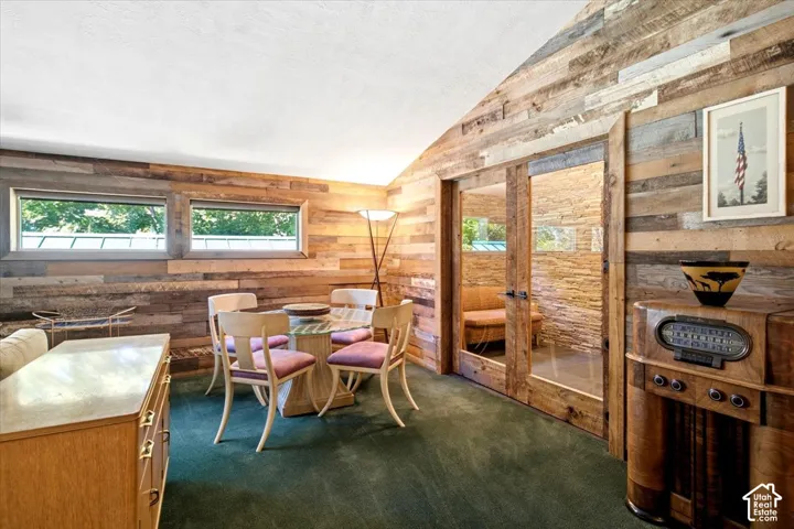 Reclaimed wood paneling, green carpeting, glass-top dining table, double glass-paneled doors, wood-finish console