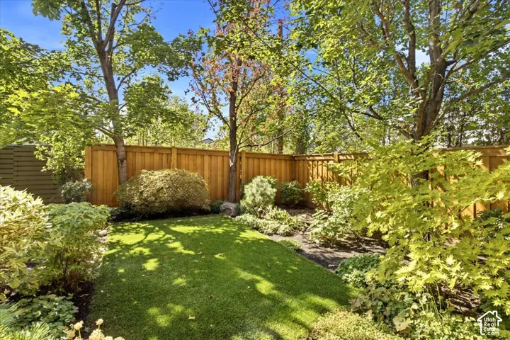 Expansive backyard featuring a manicured lawn, established perimeter landscaping, and a wood privacy fence