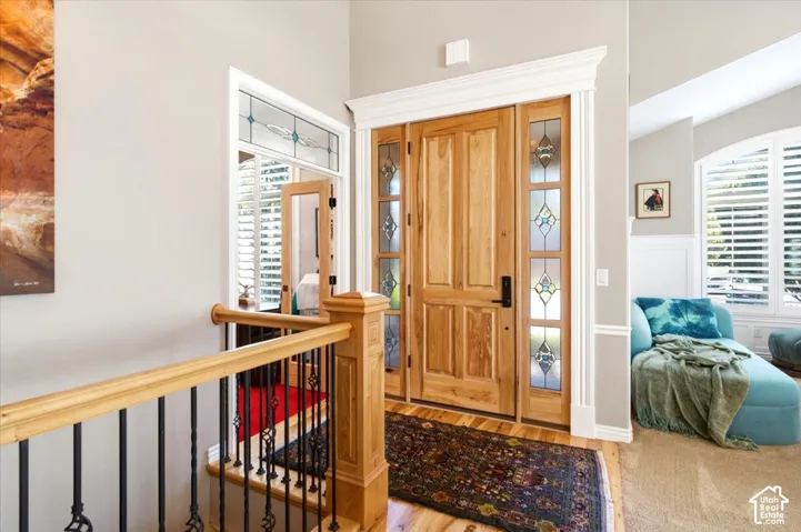 Solid wood entry door with decorative glass sidelights, white trim, and a wood staircase with wrought iron balusters