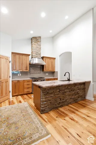 Kitchen featuring a stone-clad island with a countertop, stainless steel range with matching hood, and wood cabinetry