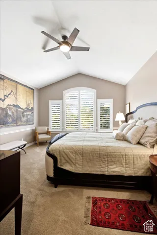 Vaulted ceiling with modern ceiling fan, arched window with plantation shutters, and light-toned carpeting