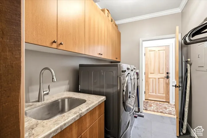 Integrated laundry area featuring wood-finish cabinetry, a utility sink with a gooseneck faucet, light-toned countertop, and durable floor tiling