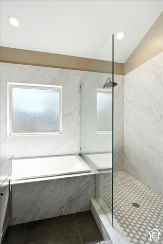 Recessed lighting illuminates the space, highlighting the built-in bathtub and the separate shower with a glass enclosure