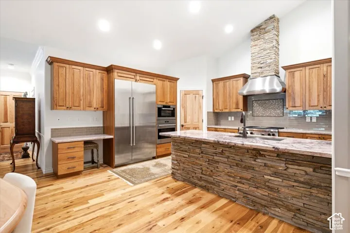 Wood-finish flooring with a stone-clad kitchen island, complemented by stainless steel appliances and wood cabinetry