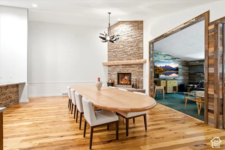 Hardwood flooring, stone-clad fireplace with mantel, recessed lighting, and a modern chandelier