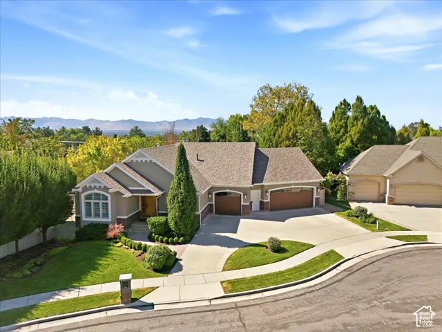 Stucco exterior with stone accents, mature landscaping, multi-car garage, and concrete driveway
