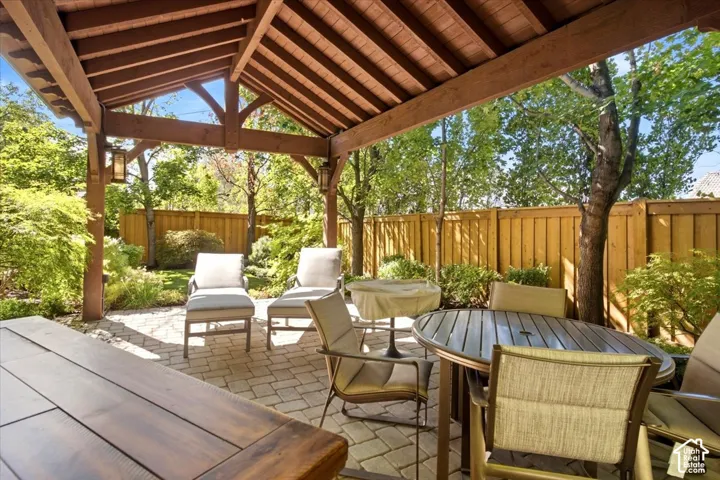Expansive patio featuring a wood-beam pergola, paver flooring, and built-in lighting fixtures