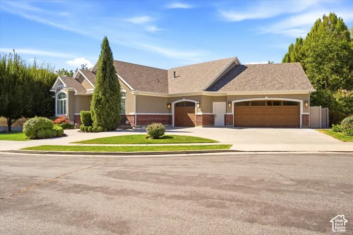 Stucco exterior with brick detailing, multi-car garage with wood-finish doors, arched windows, and a landscaped front yard