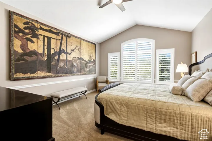 Vaulted ceiling with a ceiling fan, three windows with plantation shutters, neutral-toned wall paint, and carpet flooring